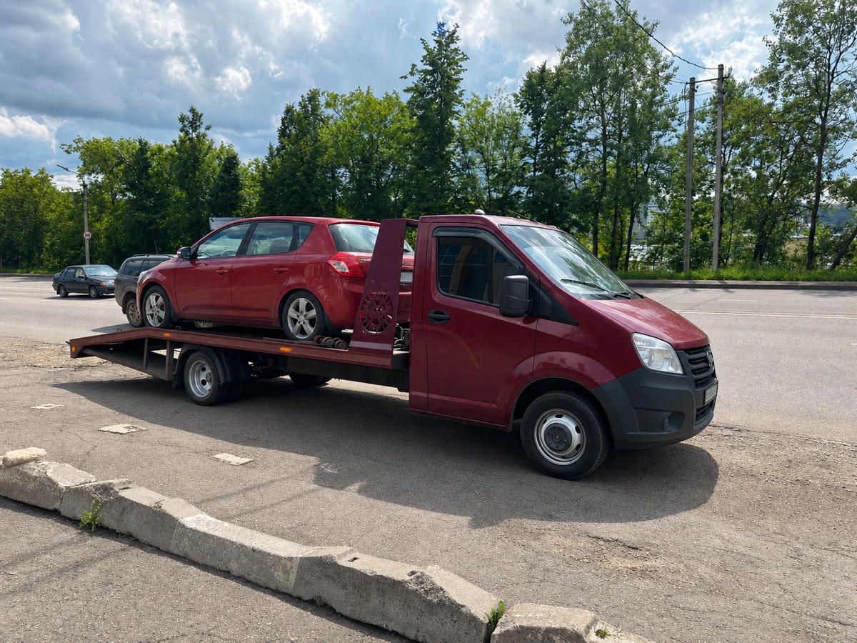 Красный автомобиль на бордовом эвакуаторе у дороги